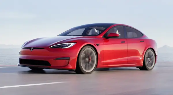 Czerwony Tesla Plaid pędzi po drodze, z widokiem na morze i góry w tle.