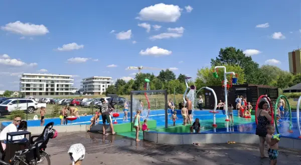 Dzieci bawią się na wodnym placu zabaw przy zalewie Borki. Woda tryska z kolorowych elementów, tworząc radosną atmosferę.