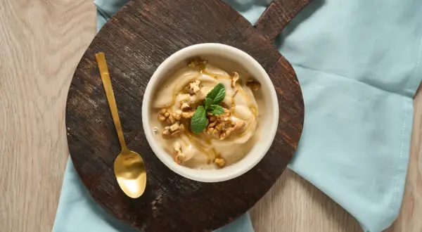 En skål med krämig nice cream, toppad med valnötter, mynta och honung. En gyllene sked ligger bredvid.