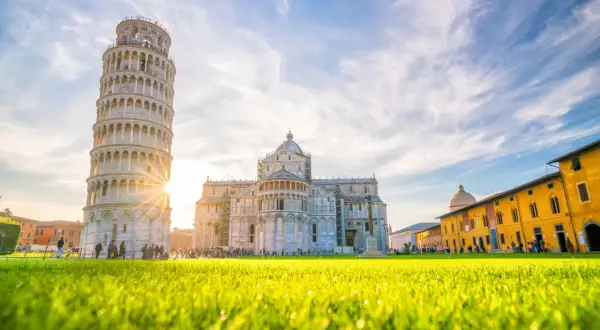 La Torre di Pisa, Italia, brilla sotto un cielo azzurro con nuvole bianche. L'erba verde brillante in primo piano cattura la luce del sole.