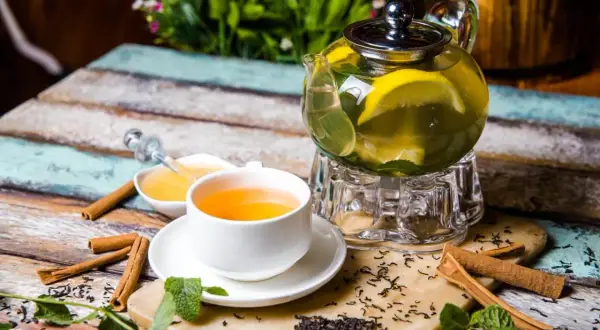 Aromatyczna zielona herbata parzenie na uspokojenie z cytryną i miodem. Na stole leżą laski cynamonu i świeża mięta.