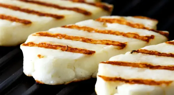 Trzy kawałki halloumi z grilla, z charakterystycznymi brązowymi paskami, leżą na czarnej, żebrowanej powierzchni.