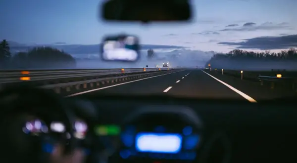 Conduite de nuit sur une autoroute italienne, respectant la limitation de vitesse. Brouillard léger, lumières des phares et du tableau de bord.