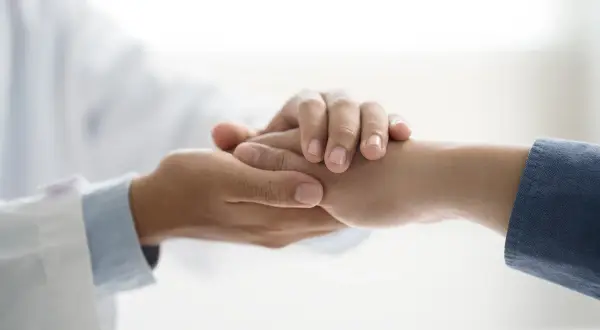 Dłoń lekarza w białym kitlu pociesza dłoń pacjenta. Symbol niepełnosprawności 02-p dofinansowanie.
