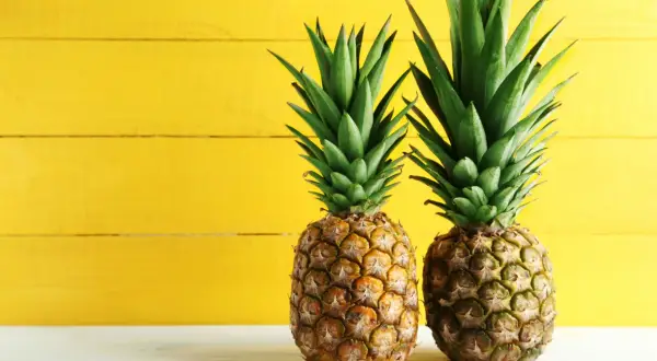 Dwa soczyste ananasy na tle żółtej deski. Poznaj ich bogactwo witamin i minerałów – ananas wartości odżywcze.
