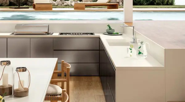 Moderna encimera para exterior con barbacoa integrada, junto a una piscina y tumbonas.