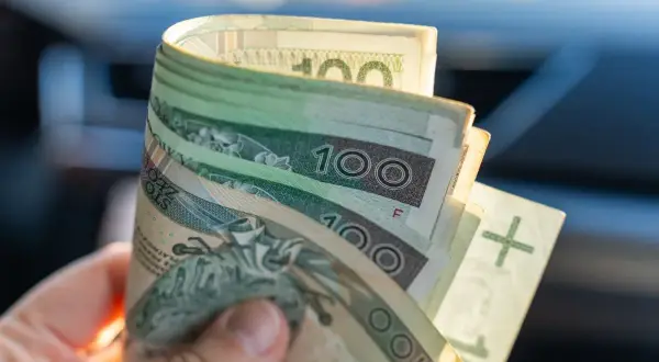 Dłoń trzyma banknoty 100 zł. Kiedy wypłata 13 i 14 emerytura 2026?