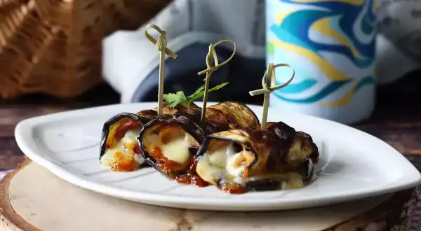 Grillad aubergine rullad med ost och tomatsås, serverad på en vit tallrik. Perfekt för picknick!