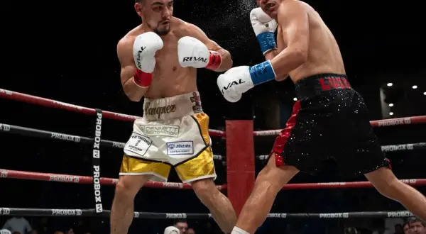 Two boxers clash in the ring. One lands a punch, sending sweat flying. This intense moment could lead to a unanimous decision in boxing if all judges score it for one fighter.