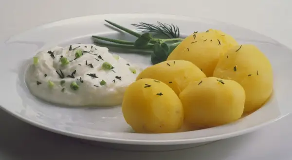 Kartoffeln mit Quark, garniert mit Schnittlauch und Dill, auf einem weißen Teller. Ein einfaches, aber köstliches Gericht.