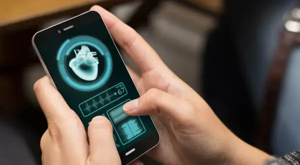Dłoń trzyma smartfon z aplikacją zdrowie, wyświetlającą obraz serca i tętno 67.