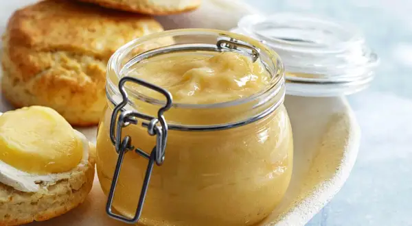En burk med hemgjord lemon curd står bredvid scones. Perfekt för ditt lemon curd recept!