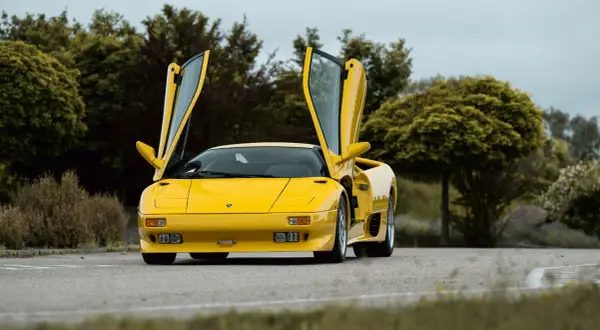 Żółty Lamborghini Diablo z otwartymi drzwiami, zaparkowany na drodze wśród zieleni.