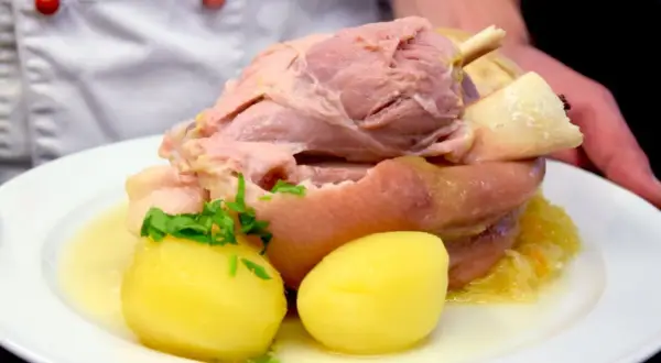 Ein deftiges Eisbein mit Sauerkraut und Kartoffeln, serviert in einem Topf.
