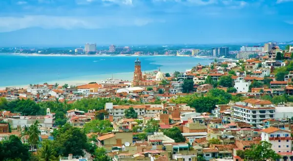 Vista panorámica de una ciudad costera en México, con casas de tejas rojas, una iglesia con cúpula y edificios modernos junto al mar azul. ¡Un sueño para vivir en México!