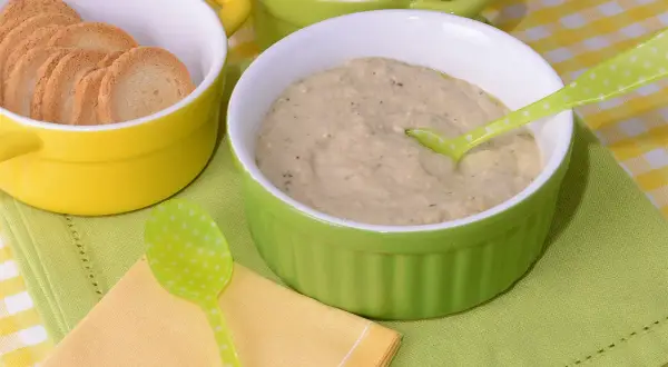 Un cremoso puré de berenjena servido en un cuenco verde, acompañado de galletas tostadas en un cuenco amarillo.