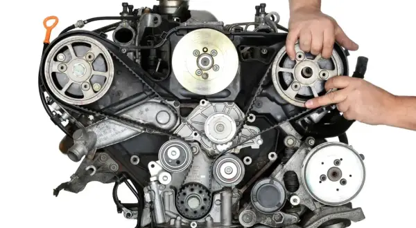 Mechanik pokazuje pasek rozrządu, kluczowy element silnika, który wymaga wymiany co określony przebieg kilometrów.