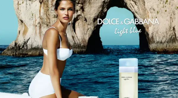 Kobieta w białym bikini na tle skalistej zatoki. Obok flakon perfum Dolce & Gabbana Light Blue.