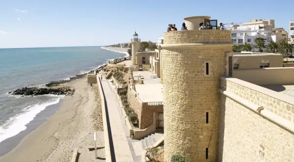 Torreón y faro en el **puerto de Roquetas de Mar**, con playa y mar Mediterráneo al fondo.