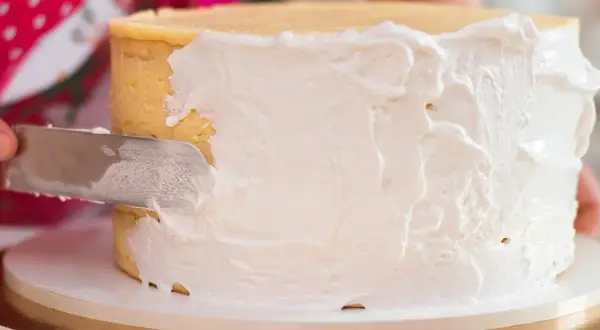Nakładanie puszystego tynku Milky Way na tort. Kremowa masa pokrywa boki ciasta, tworząc apetyczny wygląd.