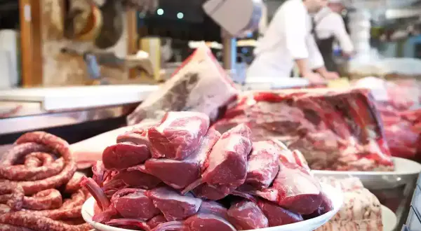Carnes grasas y magras en un puesto de carnicería. Salchichas en espiral y chuletas de cordero apiladas en platos.
