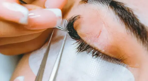 Precyzyjne przedłużanie rzęs 2-3d. Stylistka z perfekcyjnym manicurem dokłada kolejne kępki, tworząc efekt wow.
