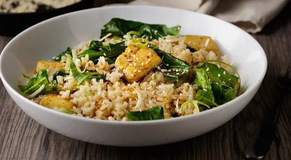 Deliciosa ensalada de arroz con trozos de tofu dorado, espinacas frescas y semillas de sésamo. Un plato nutritivo y lleno de sabor.