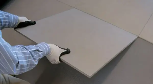 Mains gantées plaçant une nouvelle dalle pour la coller sur du carrelage existant.