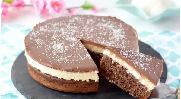 Deliziosa torta cocco e cioccolato con glassa lucida e cocco grattugiato. Una fetta è già servita.