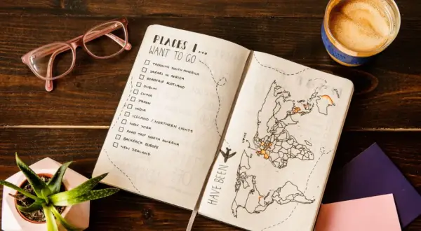 Planowanie wakacji: lista miejsc do odwiedzenia, mapa świata z zaznaczonymi podróżami, okulary i kawa.