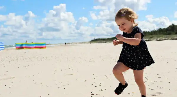 Radosne wakacje z dziećmi w Polsce. Mała dziewczynka biega po piaszczystej plaży, ciesząc się słońcem i chmurami na niebie.
