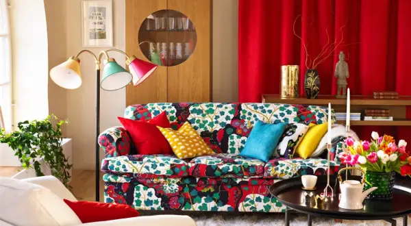 Sofá con estampado floral vibrante, cojines coloridos y una lámpara de pie que evoca un estilo vintage.