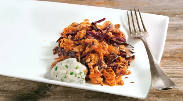 Herzhafte Krautpfanne mit Hackfleisch, serviert mit einem Klecks Kräuterquark und einer Gabel auf einem weißen Teller.