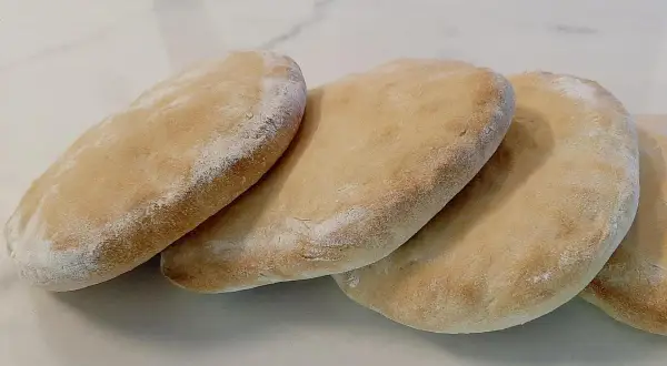 Quatre pains arabes dorés, légèrement saupoudrés de farine, prêts à être garnir.