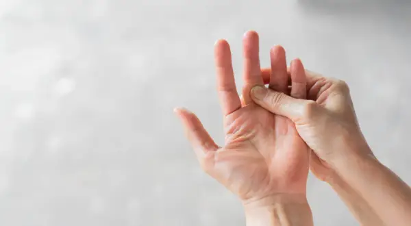 Hand massiert einen schmerzenden Finger, der auf eine Prellung hindeutet.