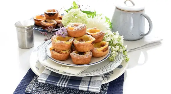 Montón de pastel de nata portugal, espolvoreados con azúcar glas, decorados con flores y servidos en platos de cerámica.