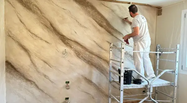 Pittore applica stucco effetto marmo su una parete, creando venature naturali.