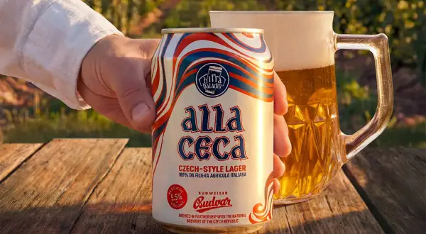 Mano che tiene una lattina di Budweiser ceca "Alla Ceca", con una birra in un boccale sullo sfondo.