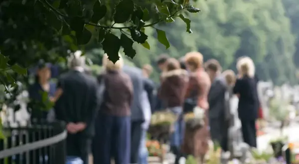 Ludzie na cmentarzu, w zadumie. Czy można pochować zmarłego w innym mieście? Pytanie, które zadaje sobie wielu.
