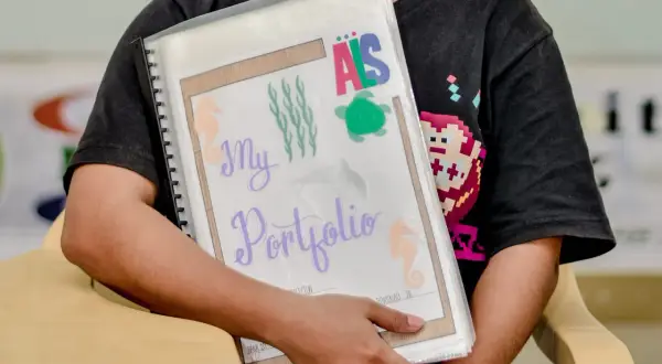 Ein Kind hält ein bunt gestaltetes Portfolio für den Kindergarten mit Seepferdchen und Schildkröten.