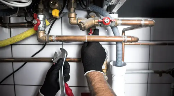 Handwerker verlegt Waschmaschinenanschluss. Kupferrohre, Ventile und Werkzeug sind zu sehen.