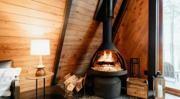 Gemütlicher Kaminofen mit Zulassung, bereit für den Schornsteinfeger. Holzscheite liegen daneben.