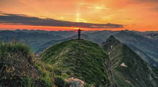 Sonnenuntergang auf der Kanisfluh Wanderung. Ein Wanderer steht mit ausgebreiteten Armen auf dem Gipfel und genießt den atemberaubenden Ausblick.