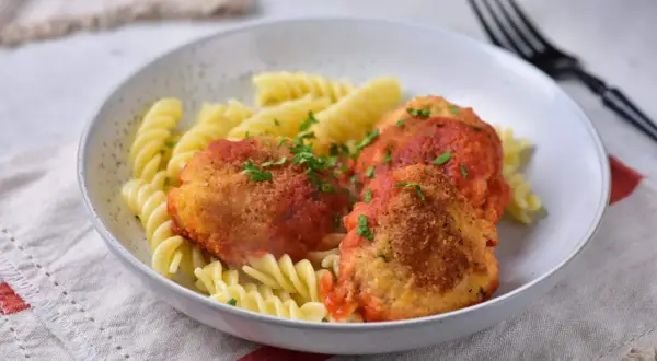 Kotlety w sosie pomidorowym z makaronem fusilli, posypane natką pietruszki.