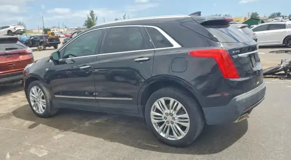 Czarny Cadillac XT5 stoi na placu wśród innych pojazdów.