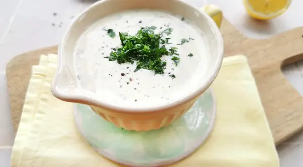 Cremige Schüssel mit frischem Ranch Dressing, garniert mit Petersilie und Pfeffer. Daneben liegen Zitronenspalten und ein Stapel Servietten.