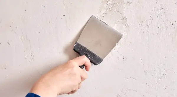 Mano con espátula realizando el alisado de paredes, preparando la superficie para un acabado perfecto.