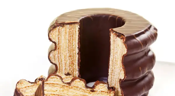 Ein angeschnittener Baumkuchen mit Schokoladenglasur, dessen Schichten die aufwendige Baumkuchen Herstellung zeigen.