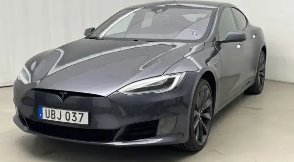 En mörkgrå Tesla Model S, en begagnad elbil med svensk registreringsskylt UBJ 037, står parkerad inomhus.