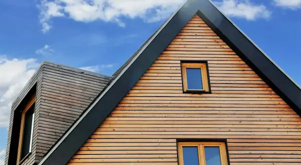 Moderne holzfassade mit horizontalen Holzlamellen und Fenstern unter blauem Himmel mit Wolken.